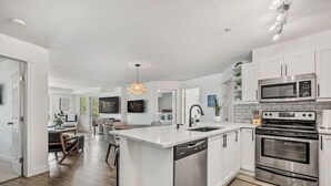 A modern kitchen with white cabinetry, stainless steel appliances, and a central island with a dishwasher. - La Bohème | Pool Views | Hot Tub | Lake Access (Invermere)