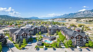 A multi-story hotel with a pool, surrounded by mountains and a parking lot. - La Bohème | Pool Views | Hot Tub | Lake Access (Invermere)