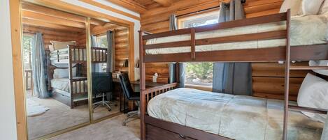Un dormitorio de cabaña de madera con literas, un escritorio y una silla.
