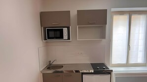 A compact kitchen with a microwave, sink, and cabinets. - Apartment in Ballon Near Le Mans Circuit (Ballon-Saint-Mars)