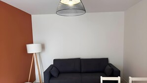 A modern living room with a black sofa, a wooden dining table, and a floor lamp. - Apartment in Ballon Near Le Mans Circuit (Ballon-Saint-Mars)