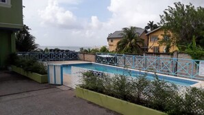 A swimming pool with a blue fence, surrounded by greenery and a view of the sea. - Luxurious Sea View From The Pool (Gulf View)
