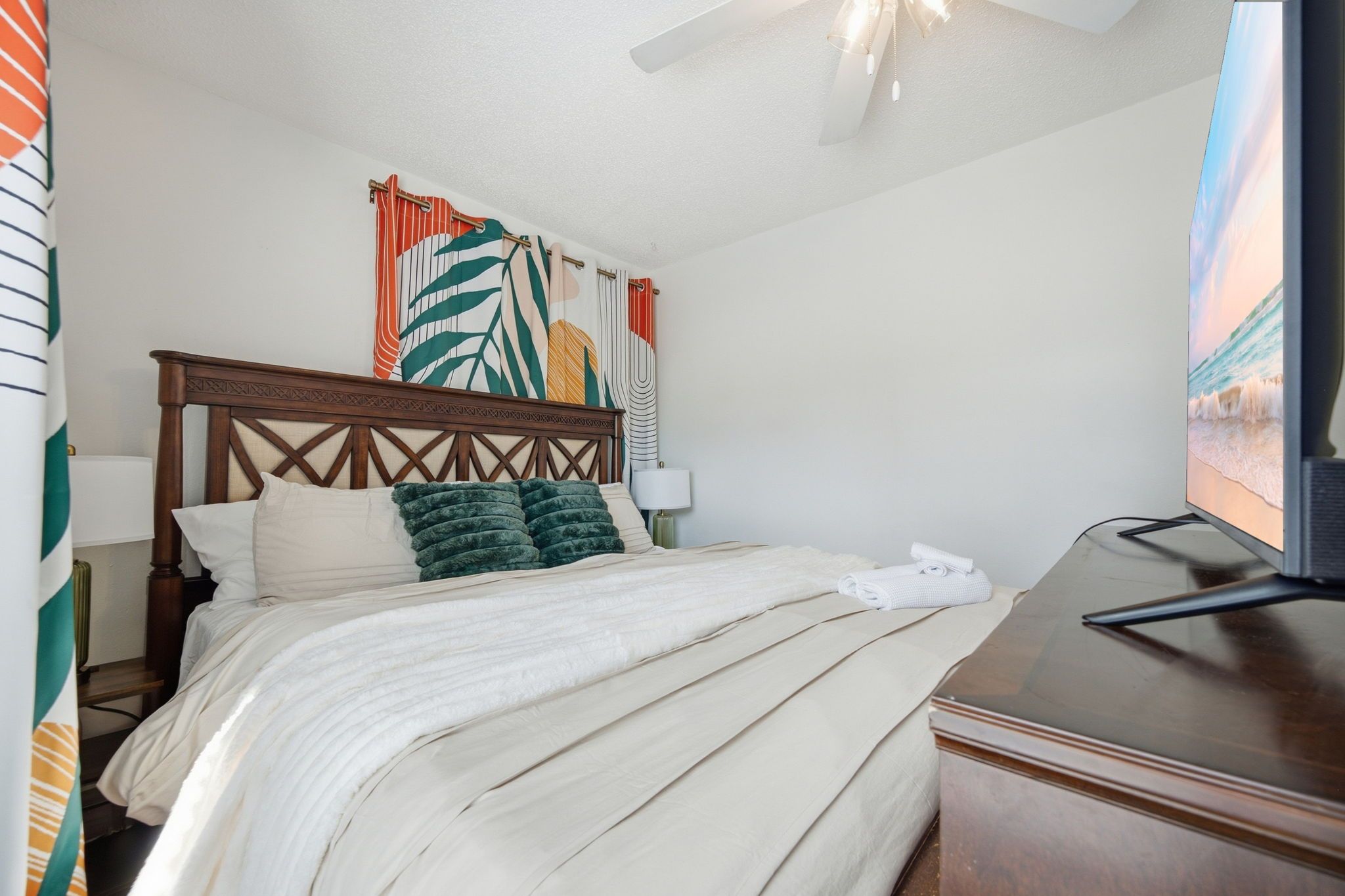 Ein Hotelzimmer mit Bett, Fernseher, Lampe und Blick aufs Meer.