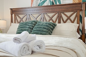 A neatly made bed with a wooden headboard, two green pillows, and rolled white towels.