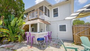 A two-story house with a balcony, a barbecue area with purple chairs, and a wooden deck.