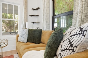 A living room with a sofa, decorative pillows, a side table, and a window with curtains.
