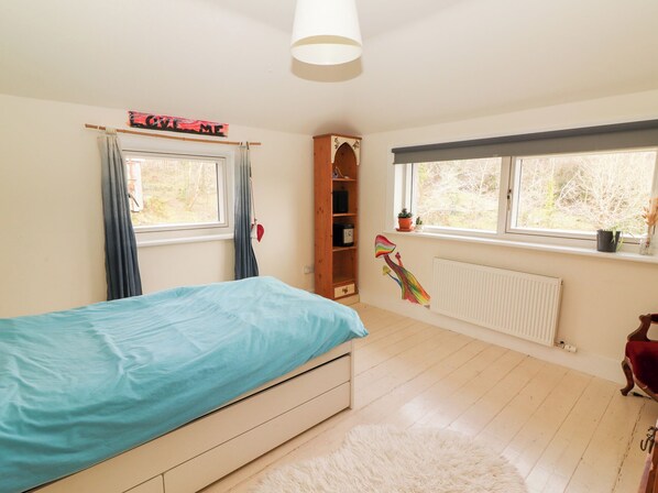 Ein Schlafzimmer mit Bett, Heizkörper, Fenster mit Aussicht, Regal mit Gegenständen und einem 'Welcome'-Schild.