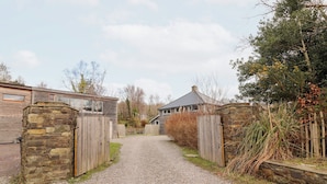 Ein unbefestigter Weg führt zu einem rustikalen Haus mit Steinmauern und Holztoren.