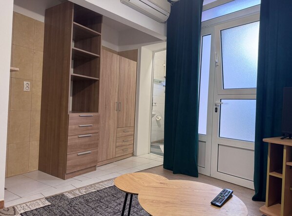 A room with a wooden wardrobe, a small round table, and a door leading to a balcony with curtains.