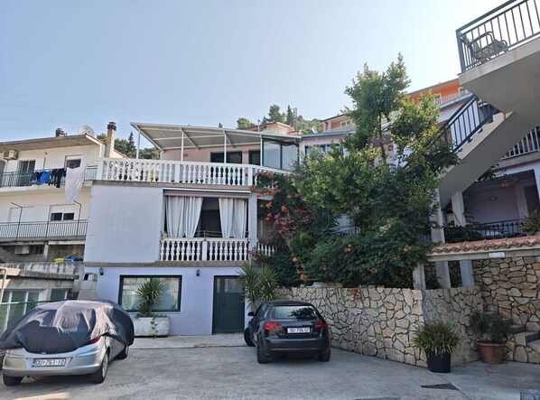 A residential building with a two-story balcony, a stone wall, and a parked car.