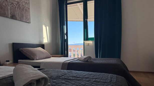 A hotel room with two beds, a view of the city, and a balcony with a railing.