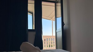 A hotel room with a bed, a rolled towel, a window with curtains, and a view of a balcony with a railing.