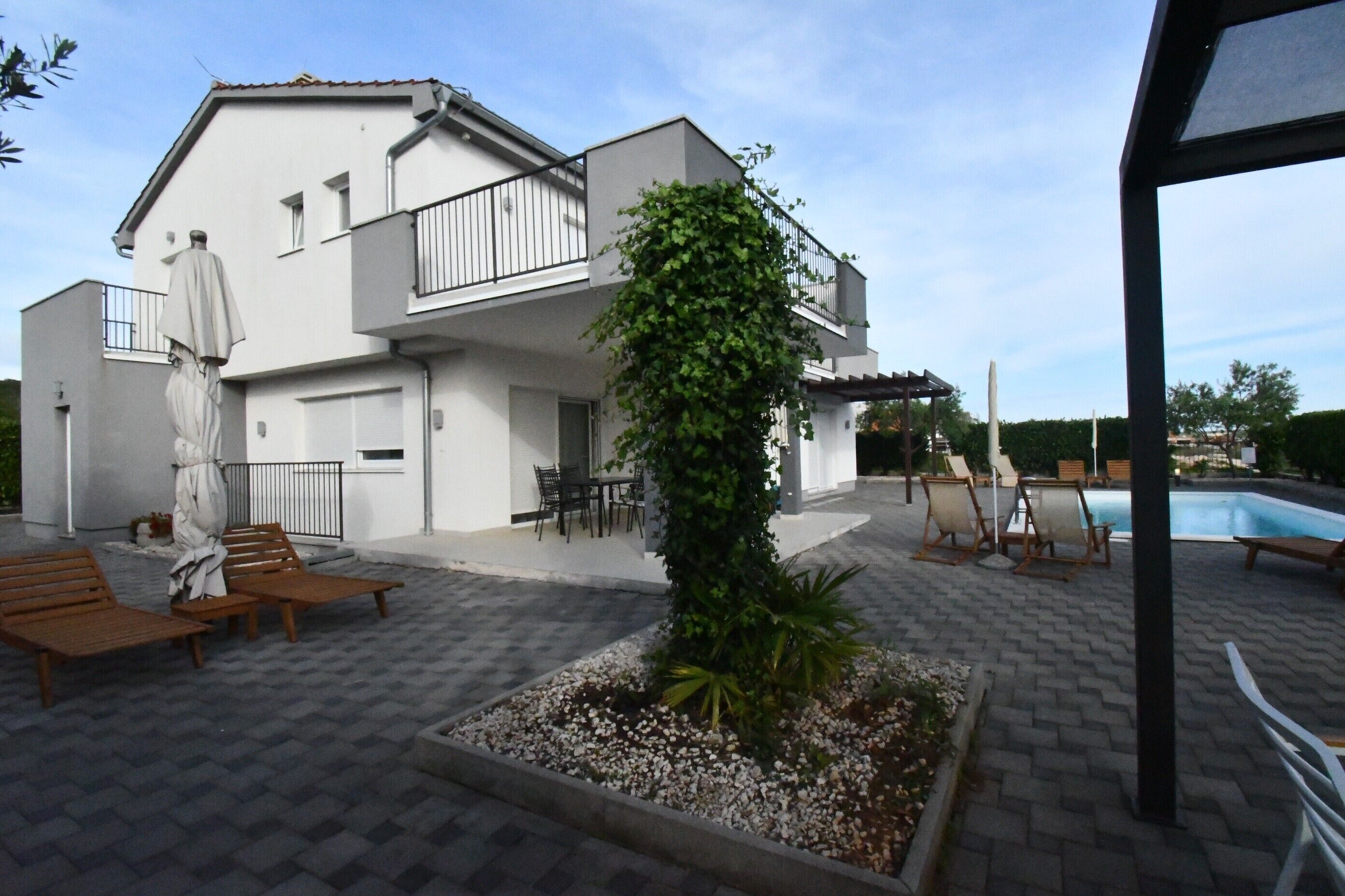 Ett modernt hus i två våningar med en uteplats, utomhusmöbler och en swimmingpool.