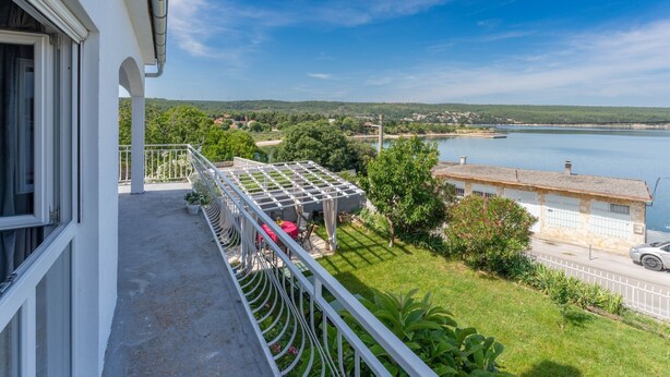 A balcony with a pergola, a view of a lake, and a distant landscape with hills.