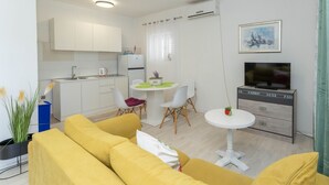 A modern living room with yellow sofas, a dining area with a small table, and a kitchen with white cabinets.