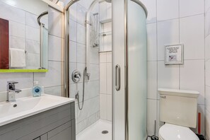 Een moderne badkamer met een glazen douchecabine, een wit toilet en een wastafel met een zeepdispenser.