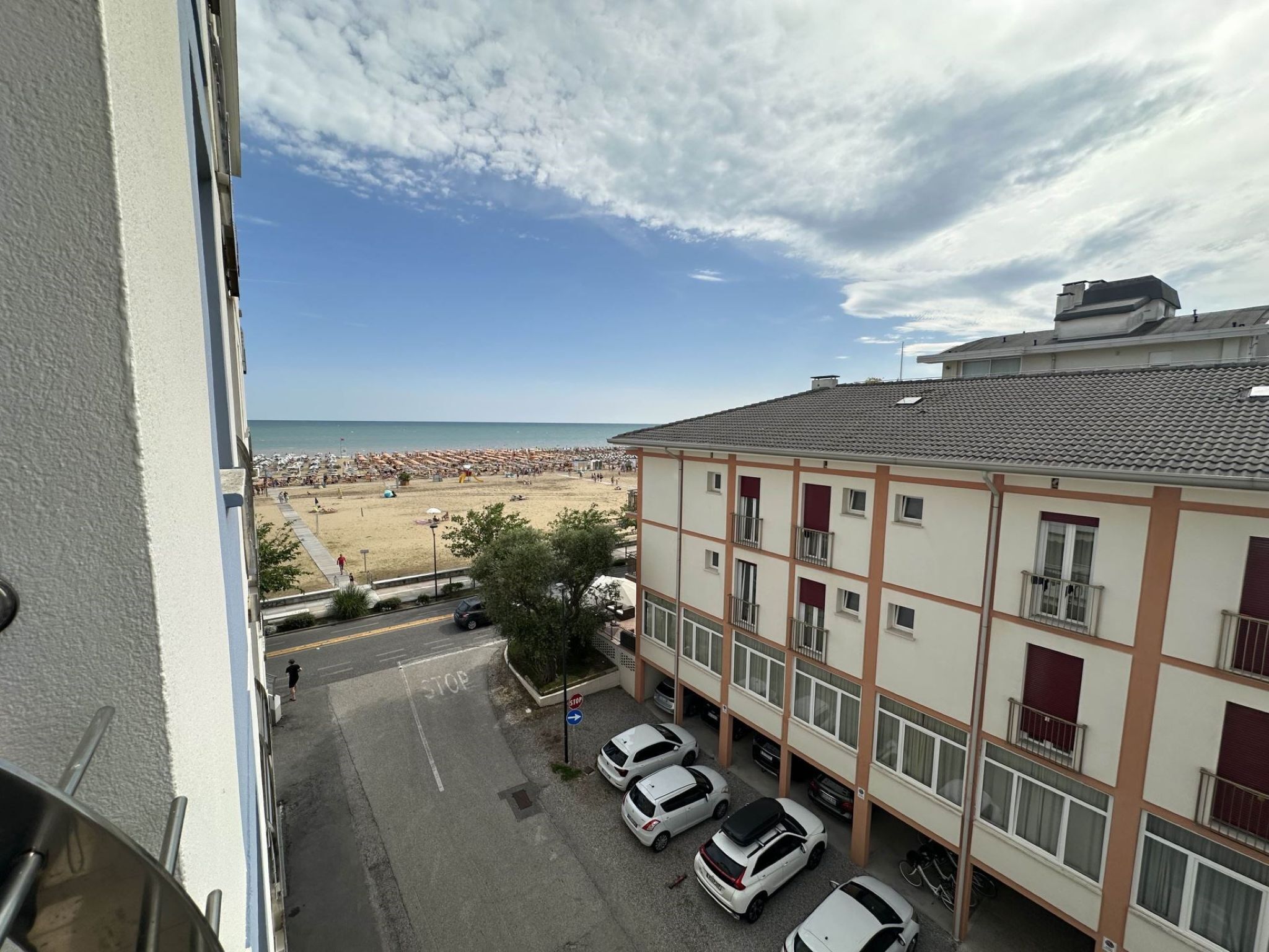 Une vue d’une plage où l’on aperçoit une rangée de voitures blanches garées devant un immeuble doté de balcons et d’un toit recouvert de tuiles.