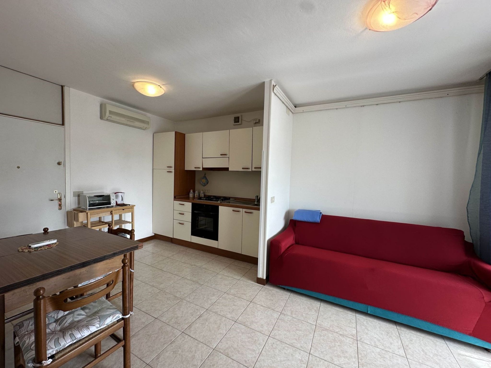 Un espacio habitable compacto con kitchenette, zona de comedor y sofá rojo.