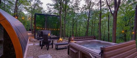 Un jacuzzi, terraza de madera y zona de estar al aire libre rodeada de árboles.