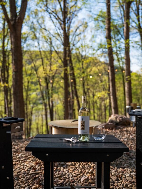 Una mesa de picnic con una botella de vino blanco, una copa y llaves en un entorno boscoso.