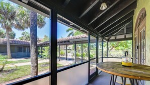A covered outdoor area with a wooden table and chairs, a yellow object on the table, and a view of a residential area with palm trees and houses.