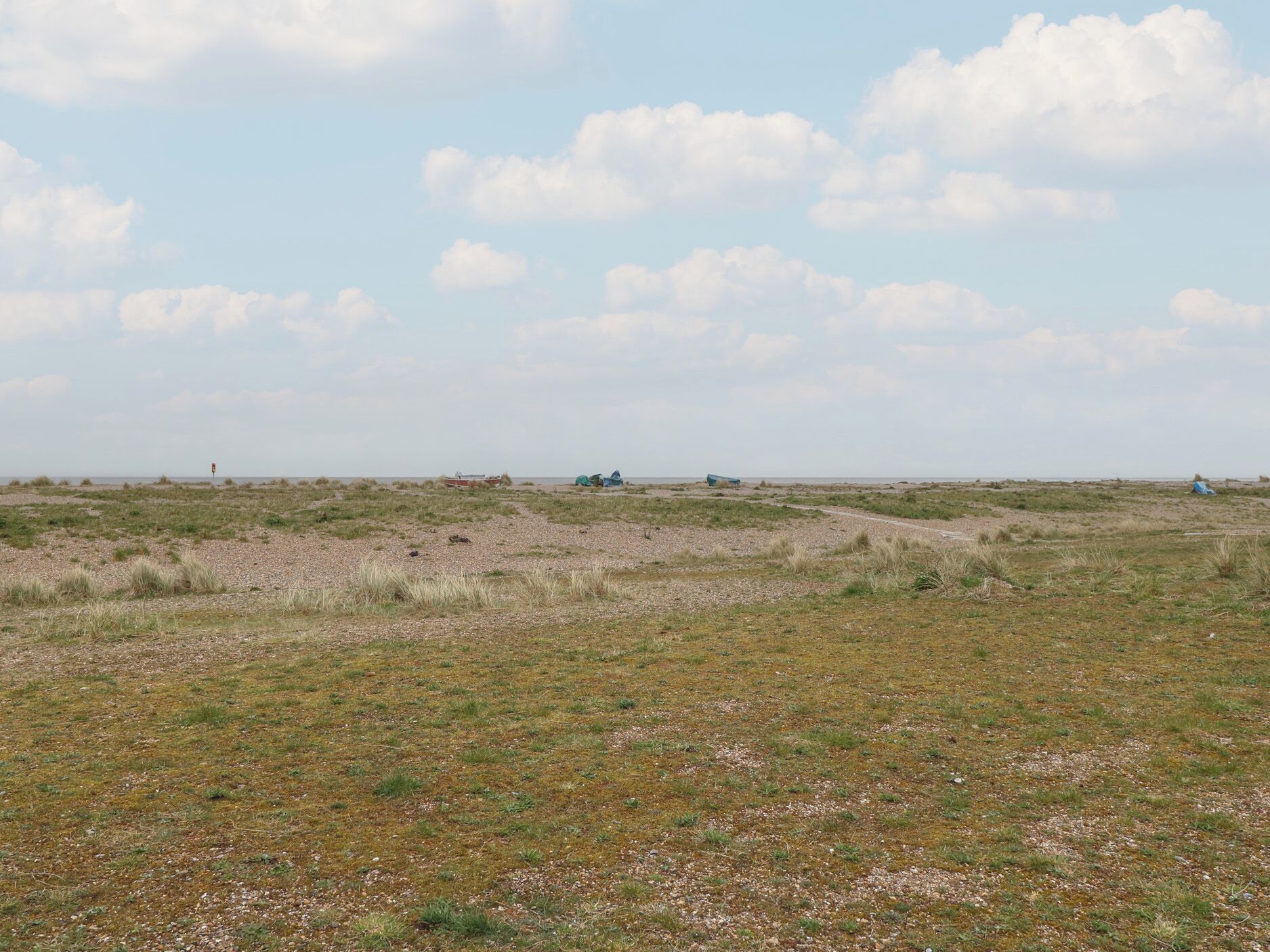 A flat, open landscape with sparse vegetation and a few scattered structures.