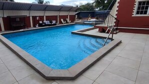 En swimmingpool med ett kaklat poolområde, en överbyggd sittplats och en trappa som leder upp till en balkong.