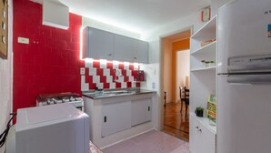 Eine kleine Küche mit rotem und weißem Fliesenspiegel, einem weißen Kühlschrank und einer Kaffeemaschine.