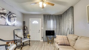 Een woonkamer met een beige bank, twee fauteuils, een televisie en een plafondventilator.