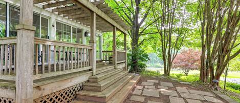 Una terraza de madera con un pérgola, un sendero de piedra y vistas a un parque con árboles y un lago.