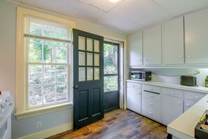 Una cocina con puerta negra, armarios blancos, microondas y ventana con persianas.