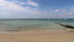 A beach with a wooden pier extending into calm waters, boats anchored in the distance, and a clear sky. - Guildford Farmhouse (Ryde)
