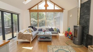A spacious living room with a high ceiling, a large window, a sofa set, a coffee table, a fireplace, and a wooden floor. - Guildford Farmhouse (Ryde)