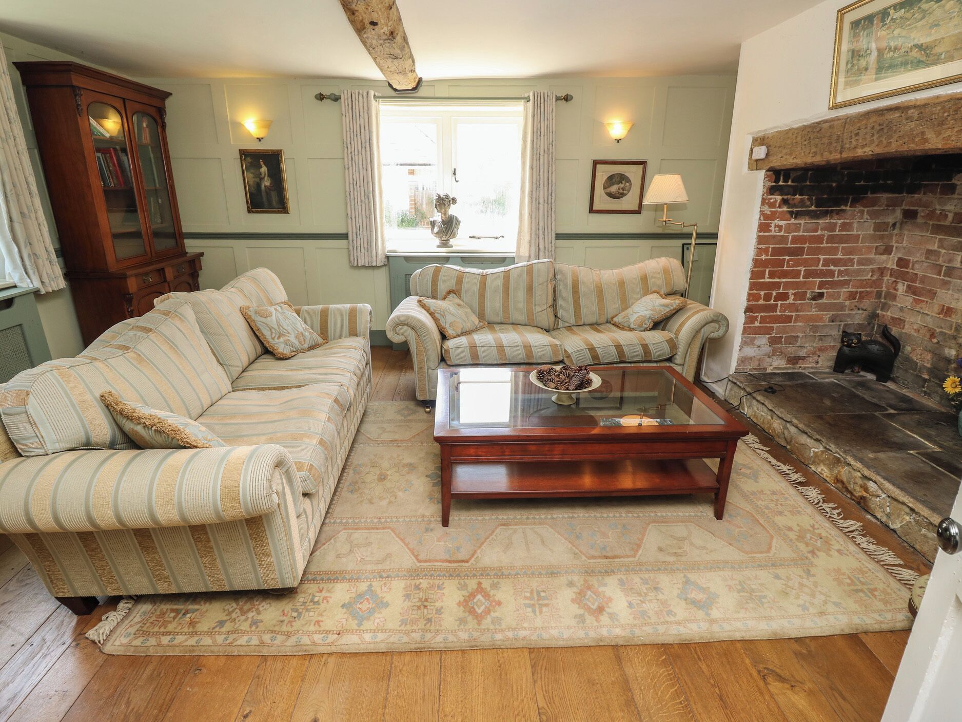 A cozy living room with striped sofas, a glass coffee table, a fireplace, and a wooden cabinet.