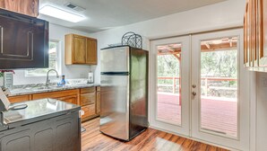 A kitchen with wooden cabinets, a stainless steel refrigerator, a sink, and a sliding glass door leading to an outdoor deck. - Walk to Lake George: Quiet Nature Escape w/ Deck (Fort McCoy)