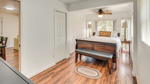 A bedroom with a wooden floor, a bed with a bench, a ceiling fan, and a window with a view of trees. - Walk to Lake George: Quiet Nature Escape w/ Deck (Fort McCoy)