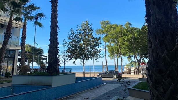 Un paseo marítimo costero con palmeras, un camino empedrado y un edificio con balcones con vistas al mar.