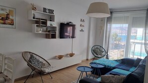 Una sala moderna con un sofá, dos sillones, un televisor y un ventanal con vistas.
