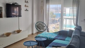 Una sala de estar moderna con sofá, televisión, lámpara colgante, sillón y vistas al exterior.