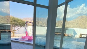 Un intérieur moderne avec de grandes fenêtres donnant sur une piscine et des montagnes.