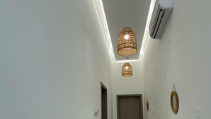 Un couloir avec un climatiseur fixé au plafond, un luminaire suspendu en fibres tressées et une porte au fond.