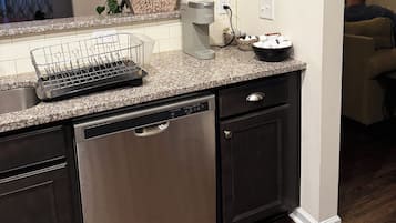 A kitchen with a built-in dishwasher, a coffee maker, and a potted plant on the counter.
