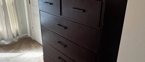 A dark wooden dresser with multiple drawers, a framed picture on the wall, and a white door in the background.