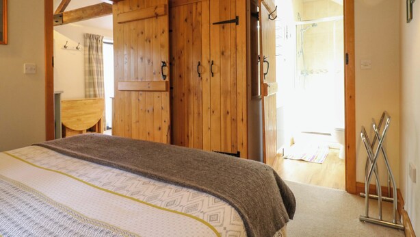A bedroom with a wooden wardrobe, a bed with a patterned bedspread, and a metal rack against the wall.
