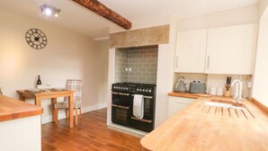 A kitchen with a wooden countertop, a stove, cabinets, and a dining area with a table and chairs. - Cottage Round T'corner (Holmfirth)