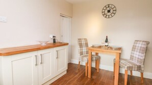 A dining area with a wooden table, two plaid chairs, a wall clock, and a white cabinet with drawers. - Cottage Round T'corner (Holmfirth)