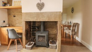 A cozy living room with a stone fireplace, a dining area with a table and chairs, and a bookshelf with books and decorative items. - Cottage Round T'corner (Holmfirth)