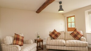 A living room with two sofas, a small table, and a hanging light fixture. - Cottage Round T'corner (Holmfirth)