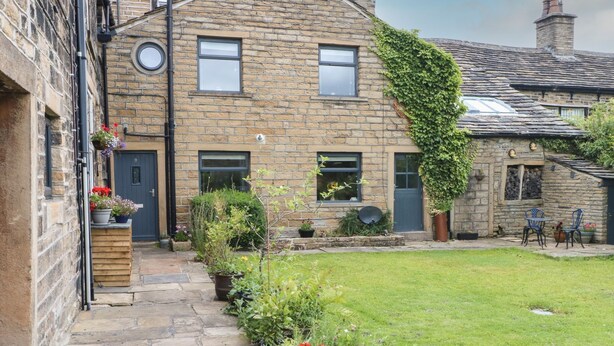 A stone building with a garden in front, featuring a stone pathway, potted plants, and a small lawn. - Cottage Round T'corner (Holmfirth)