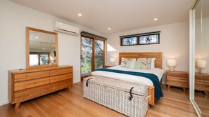 A modern bedroom with a wooden dresser, a large bed with a wooden headboard, a wicker chest, and a nightstand with a lamp. - Pet Friendly - Hopewell House with Spa and Golf Course Views (St Andrews Beach)